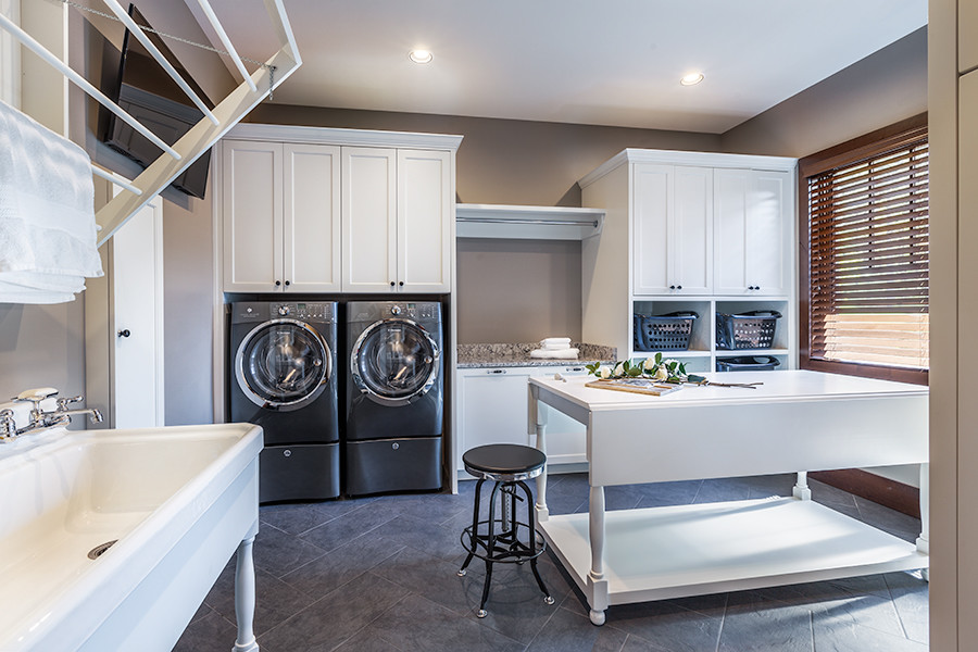 Réalisation d'une buanderie chalet multi-usage avec un évier utilitaire, des portes de placard blanches, un plan de travail en quartz modifié, un mur gris, un sol en carrelage de porcelaine et des machines côte à côte.