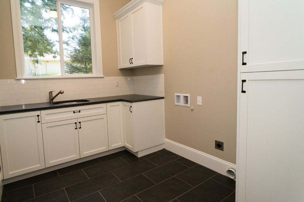 Example of a mid-sized transitional l-shaped slate floor dedicated laundry room design in Portland with an undermount sink, recessed-panel cabinets, white cabinets, granite countertops, beige walls and a side-by-side washer/dryer
