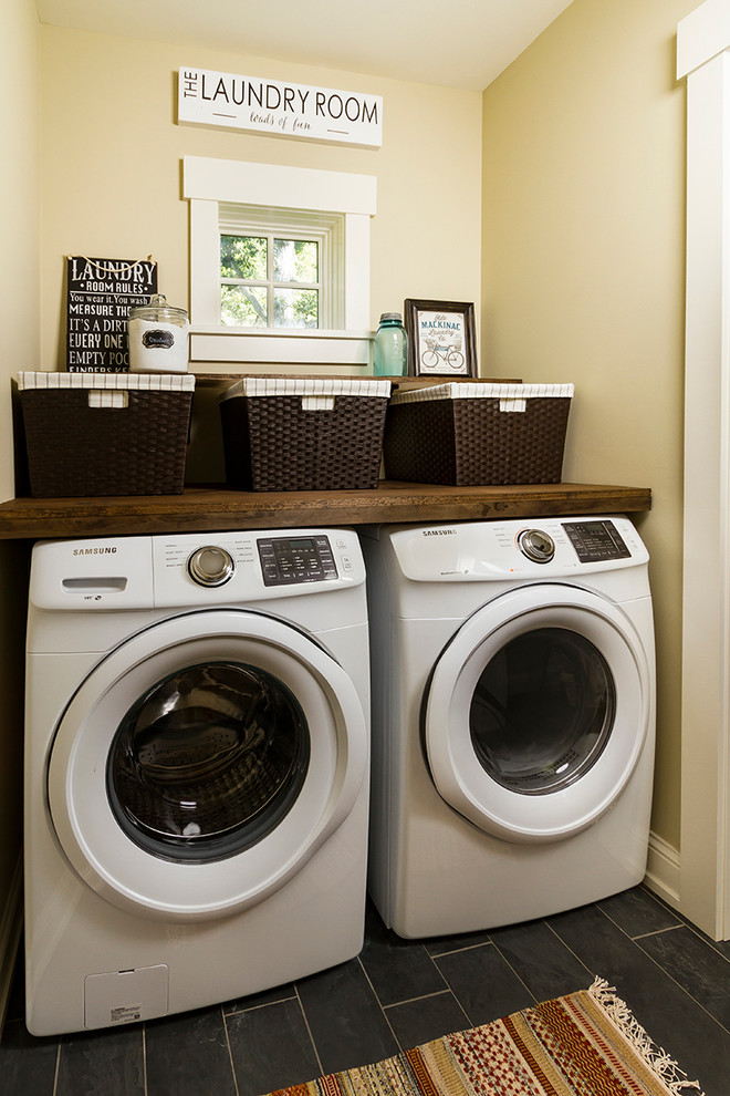 Exempel på en mellanstor klassisk linjär tvättstuga enbart för tvätt, med träbänkskiva, beige väggar, skiffergolv och en tvättmaskin och torktumlare bredvid varandra