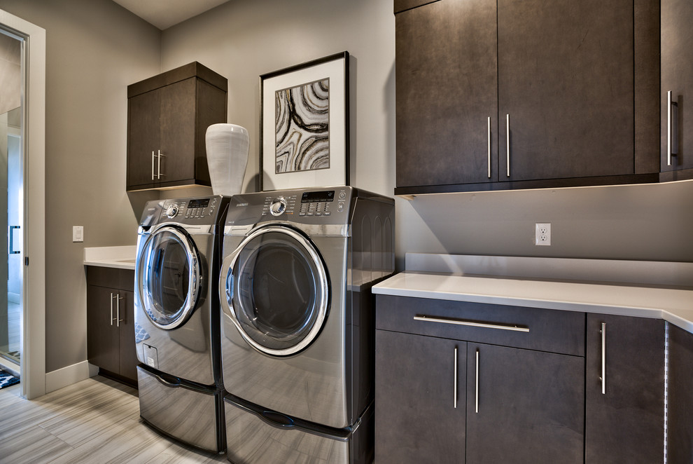 Idéer för att renovera en funkis vita l-formad vitt tvättstuga enbart för tvätt, med en undermonterad diskho, en tvättmaskin och torktumlare bredvid varandra, släta luckor, bruna skåp, grå väggar och grått golv