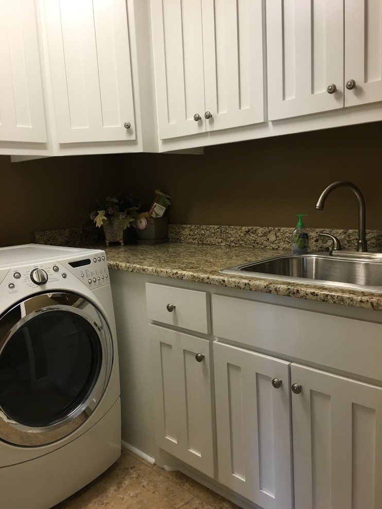 Foto på en liten amerikansk l-formad tvättstuga enbart för tvätt, med en nedsänkt diskho, luckor med infälld panel, vita skåp, granitbänkskiva, gröna väggar, klinkergolv i keramik, en tvättmaskin och torktumlare bredvid varandra och beiget golv