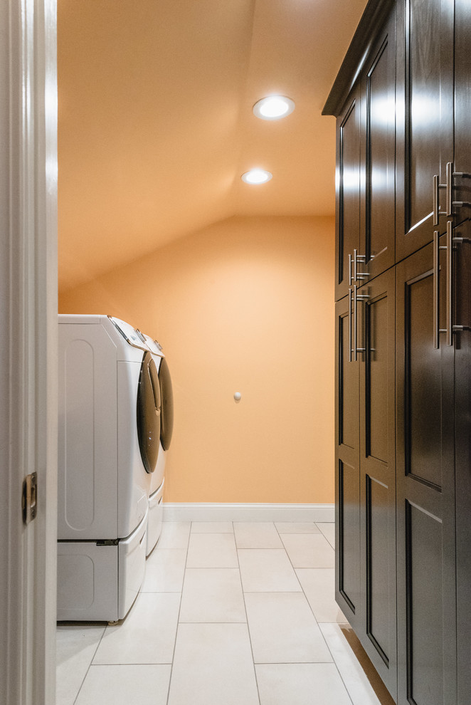Zweizeilige, Mittelgroße Moderne Waschküche mit Schrankfronten mit vertiefter Füllung, dunklen Holzschränken, Quarzwerkstein-Arbeitsplatte, oranger Wandfarbe, Porzellan-Bodenfliesen, Waschmaschine und Trockner nebeneinander, grauem Boden und weißer Arbeitsplatte in Detroit