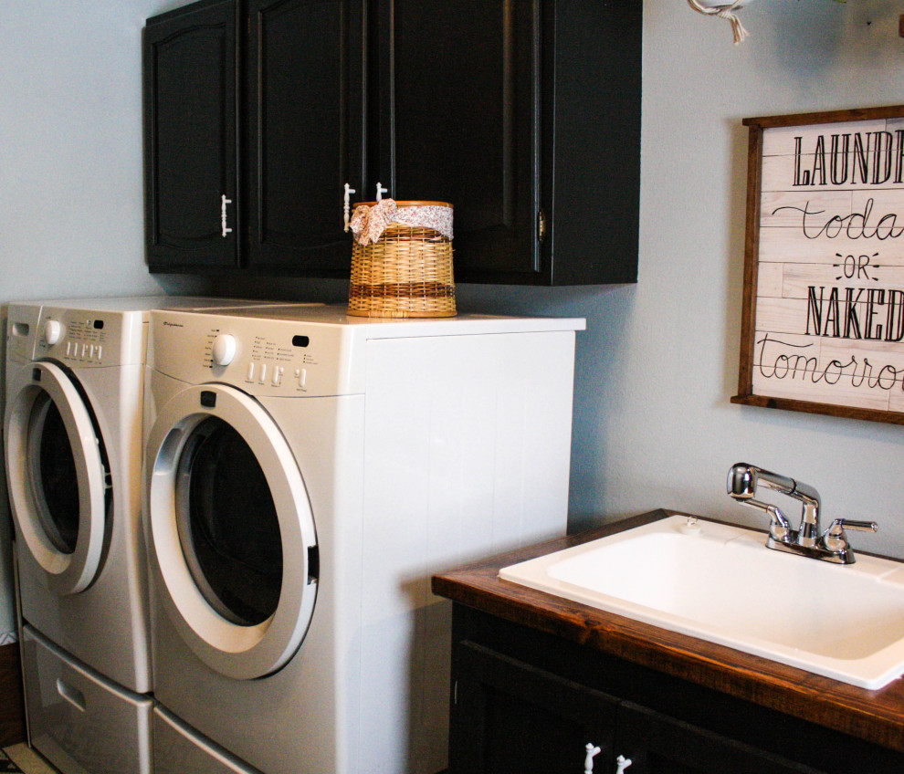 Idéer för en mellanstor industriell bruna linjär tvättstuga enbart för tvätt, med en allbänk, skåp i shakerstil, svarta skåp, träbänkskiva, blå väggar, linoleumgolv, en tvättmaskin och torktumlare bredvid varandra och beiget golv