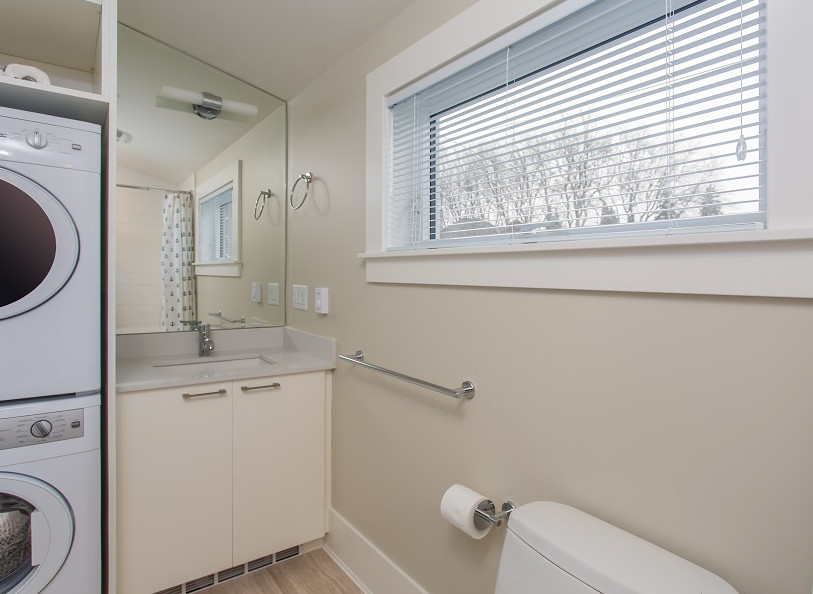 Photo of a traditional utility room in Vancouver with a submerged sink, flat-panel cabinets, white cabinets, beige walls, a stacked washer and dryer and beige floors.