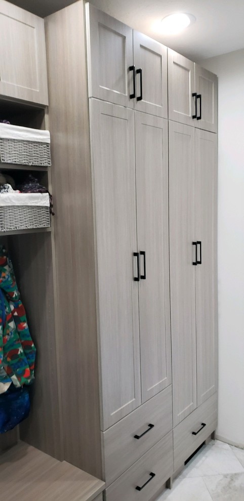 This is an example of a medium sized traditional u-shaped utility room in Indianapolis with shaker cabinets, grey cabinets, white walls, a stacked washer and dryer and grey floors.