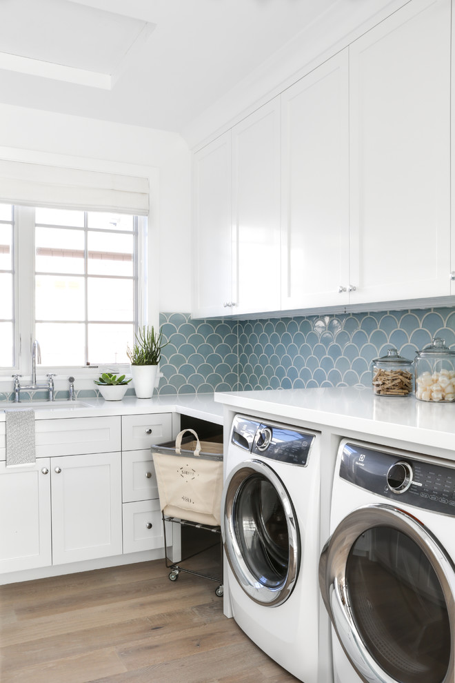 Design ideas for a coastal separated utility room in Orange County with a submerged sink, shaker cabinets, white cabinets, white walls, medium hardwood flooring, a side by side washer and dryer, brown floors and white worktops.