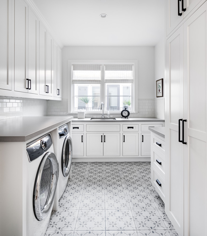 Idéer för maritima u-formade grått tvättstugor enbart för tvätt, med en undermonterad diskho, skåp i shakerstil, vita skåp, vita väggar, en tvättmaskin och torktumlare bredvid varandra och flerfärgat golv