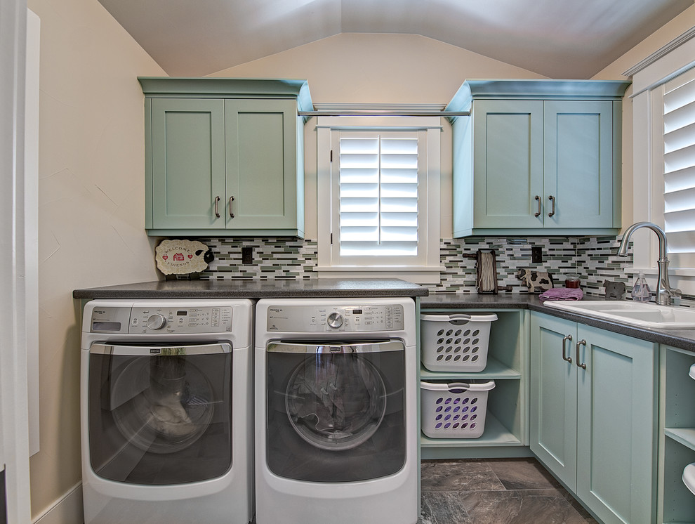 Idéer för en klassisk l-formad tvättstuga enbart för tvätt, med en nedsänkt diskho, skåp i shakerstil, blå skåp, en tvättmaskin och torktumlare bredvid varandra och beige väggar