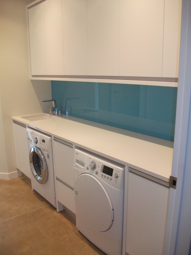 This is an example of a medium sized contemporary single-wall separated utility room in Auckland with a submerged sink, white cabinets, engineered stone countertops, white walls, dark hardwood flooring and a side by side washer and dryer.