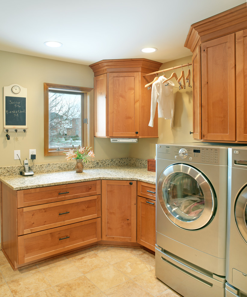 Bild på en vintage tvättstuga, med skåp i mellenmörkt trä, granitbänkskiva, klinkergolv i keramik, en tvättmaskin och torktumlare bredvid varandra, skåp i shakerstil och beige väggar