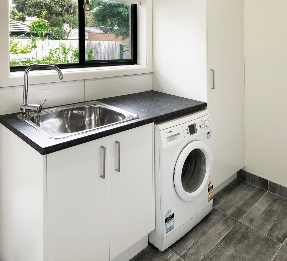 This is an example of a small modern single-wall separated utility room in Melbourne with a single-bowl sink, white cabinets, laminate countertops, white walls, porcelain flooring, an integrated washer and dryer, grey floors and black worktops.
