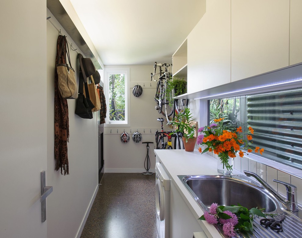 Immagine di una lavanderia multiuso design di medie dimensioni con lavello da incasso, ante bianche, top in laminato, pareti bianche, pavimento in cemento, lavatrice e asciugatrice affiancate e pavimento grigio