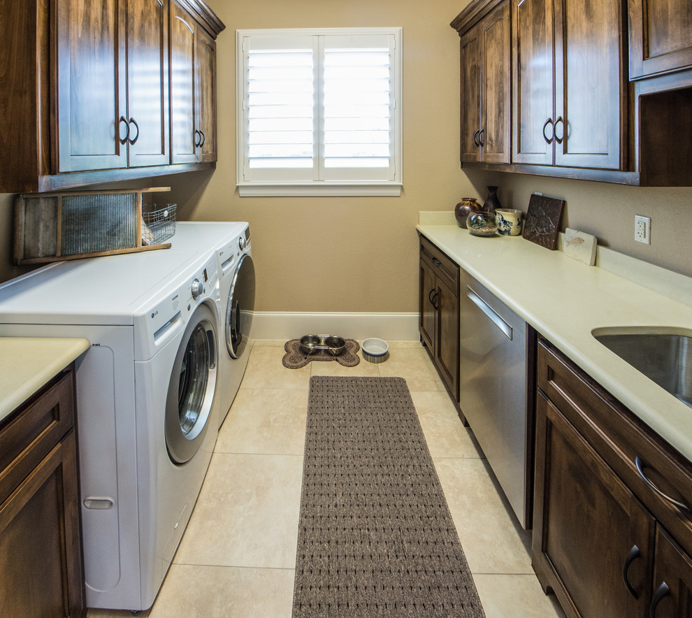Zweizeilige, Große Klassische Waschküche mit Unterbauwaschbecken, Schrankfronten im Shaker-Stil, dunklen Holzschränken, brauner Wandfarbe, Keramikboden, Waschmaschine und Trockner nebeneinander und beigem Boden in Dallas