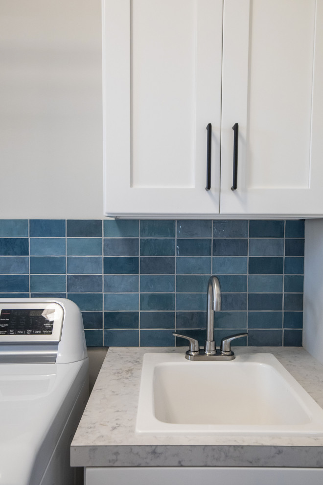 Exempel på en modern l-formad tvättstuga, med en nedsänkt diskho, skåp i shakerstil, vita skåp, laminatbänkskiva, blått stänkskydd, stänkskydd i keramik, grå väggar, vinylgolv, en tvättmaskin och torktumlare bredvid varandra och grått golv