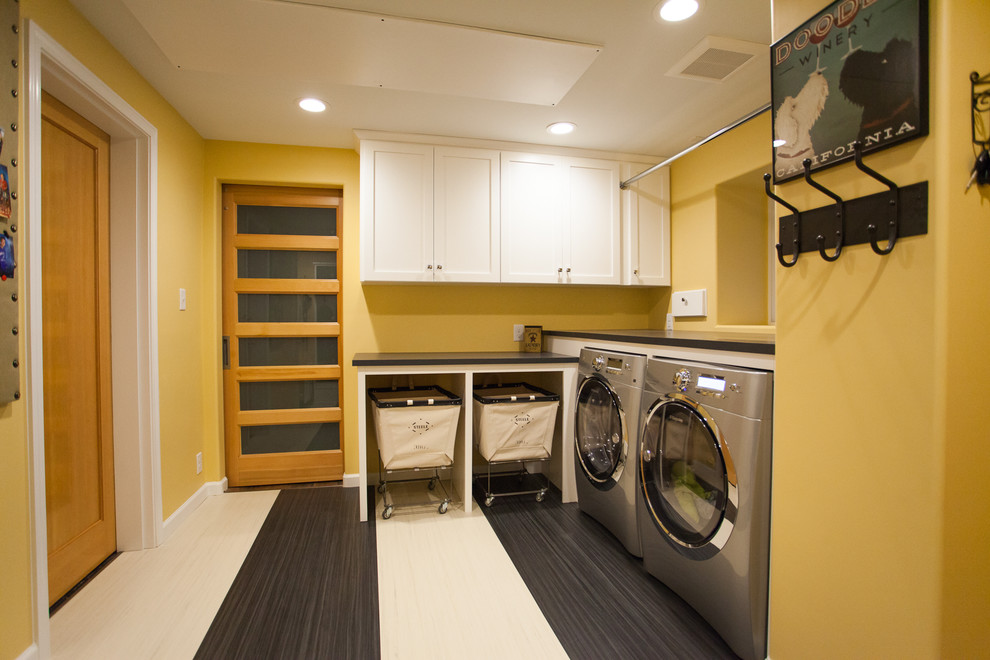 シアトルにあるお手頃価格の広いトランジショナルスタイルのおしゃれな家事室 (L型、シェーカースタイル扉のキャビネット、白いキャビネット、ラミネートカウンター、黄色い壁、リノリウムの床、左右配置の洗濯機・乾燥機) の写真
