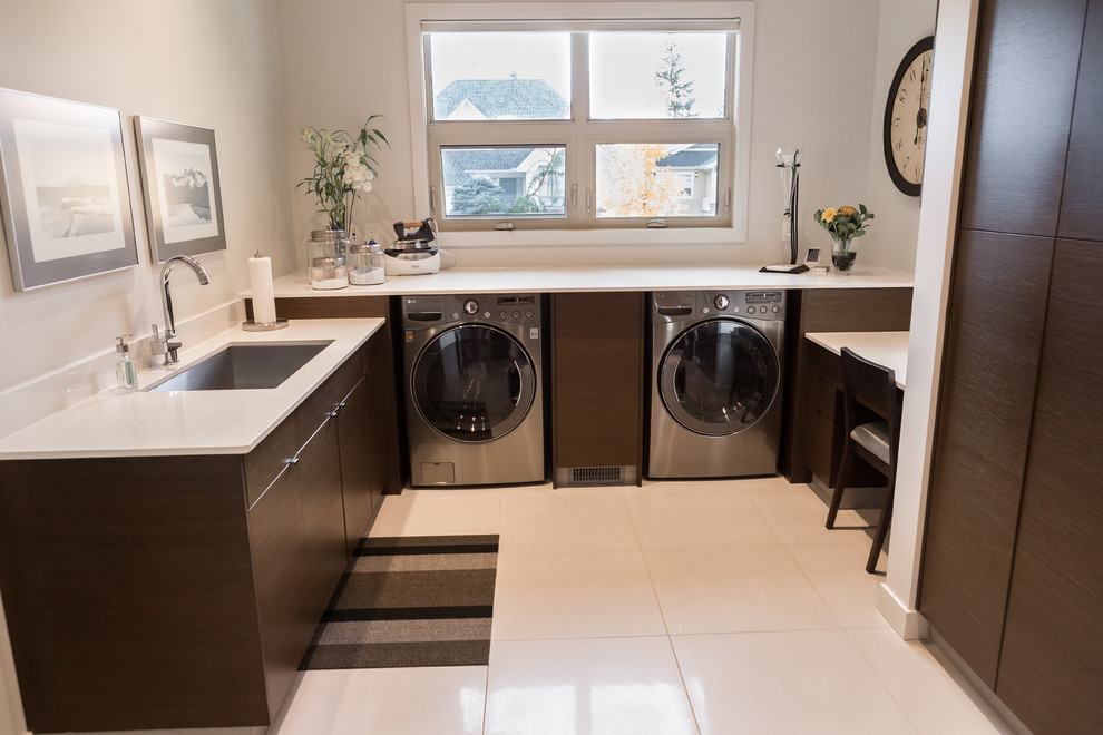 Dedicated laundry room - mid-sized contemporary u-shaped dedicated laundry room idea in Edmonton with an undermount sink, flat-panel cabinets, dark wood cabinets, solid surface countertops, white walls and a side-by-side washer/dryer