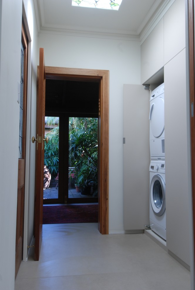 Imagen de armario lavadero lineal contemporáneo pequeño con armarios con paneles lisos, paredes blancas y lavadora y secadora apiladas
