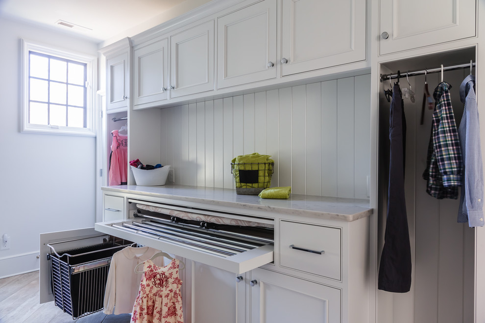 Foto di una sala lavanderia classica con ante con riquadro incassato, ante bianche, top in granito, pareti bianche, parquet chiaro e lavatrice e asciugatrice affiancate