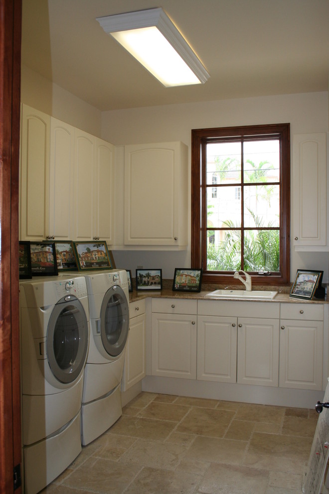 Idéer för att renovera en mellanstor vintage l-formad tvättstuga enbart för tvätt, med en nedsänkt diskho, luckor med upphöjd panel, vita skåp, granitbänkskiva, vita väggar, travertin golv och en tvättmaskin och torktumlare bredvid varandra