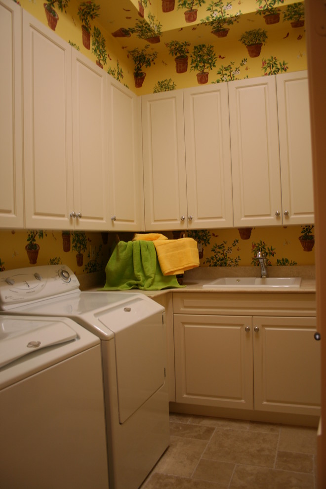 Idéer för mellanstora vintage l-formade tvättstugor enbart för tvätt, med en nedsänkt diskho, luckor med upphöjd panel, vita skåp, granitbänkskiva, flerfärgade väggar, travertin golv och en tvättmaskin och torktumlare bredvid varandra