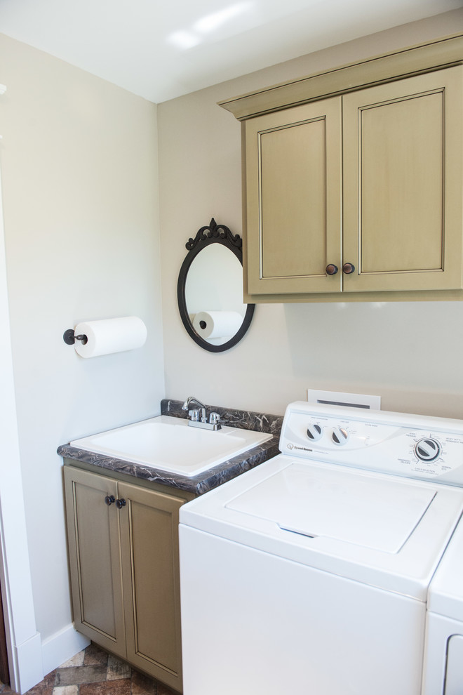 Exempel på en mellanstor lantlig parallell tvättstuga enbart för tvätt, med en nedsänkt diskho, släta luckor, gröna skåp, laminatbänkskiva, grå väggar, tegelgolv, en tvättmaskin och torktumlare bredvid varandra och flerfärgat golv