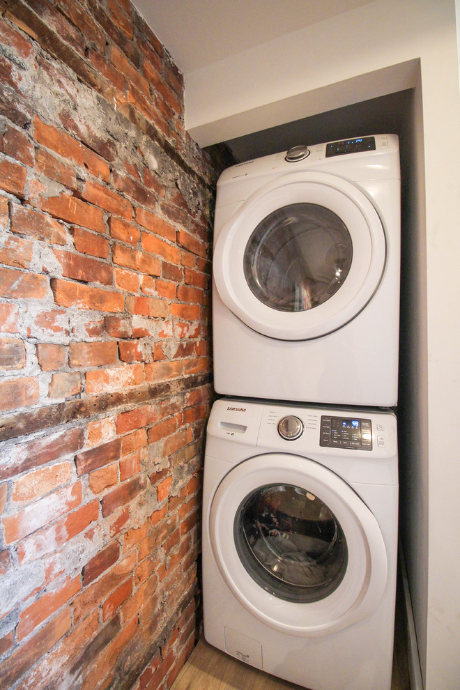 Modelo de cuarto de lavado lineal industrial pequeño con paredes blancas, suelo laminado, lavadora y secadora apiladas y suelo marrón