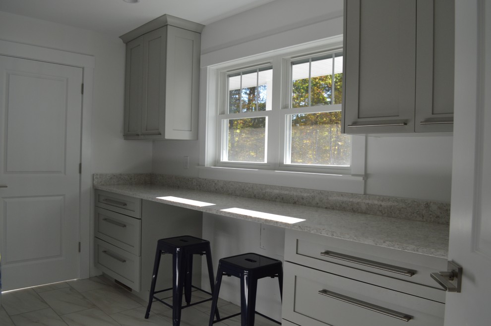 Design ideas for a medium sized classic galley utility room in Boston with a belfast sink, shaker cabinets, grey cabinets, engineered stone countertops, white walls, porcelain flooring, a side by side washer and dryer and grey floors.
