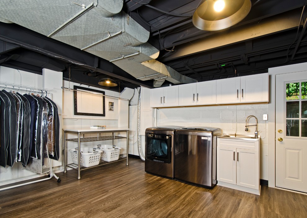 Bild på ett mellanstort industriellt grovkök, med skåp i shakerstil, vita skåp, vita väggar, laminatgolv, en tvättmaskin och torktumlare bredvid varandra, brunt golv och en nedsänkt diskho