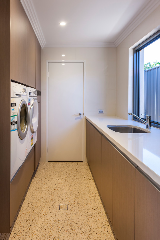 Zweizeilige, Kleine Moderne Waschküche mit Ausgussbecken, hellbraunen Holzschränken, Quarzwerkstein-Arbeitsplatte und Waschmaschine und Trockner nebeneinander in Perth