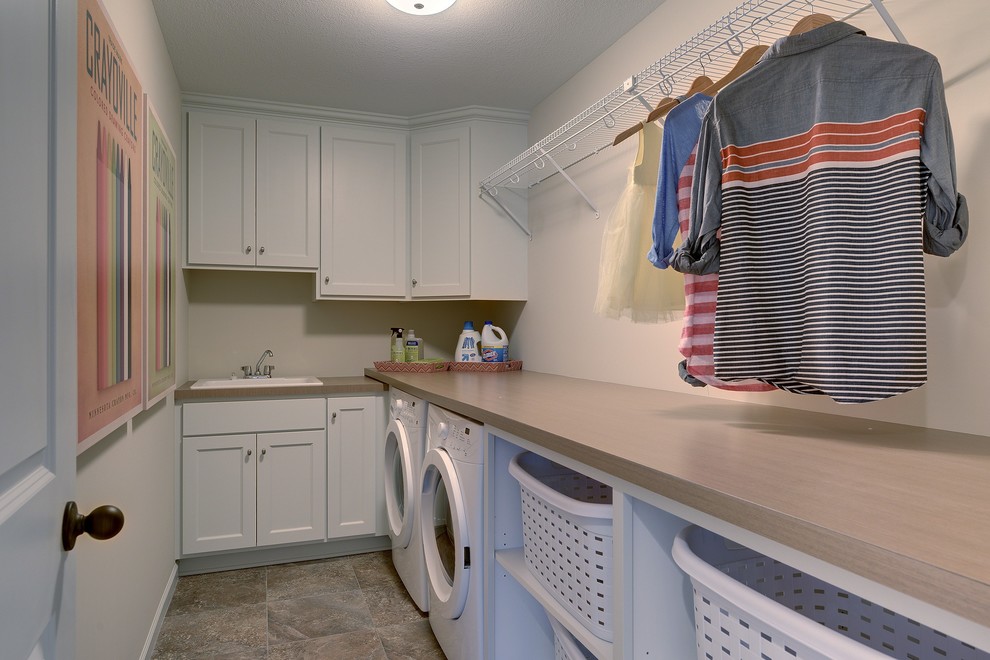 Modelo de cuarto de lavado en L tradicional renovado grande con fregadero encastrado, armarios con paneles empotrados, puertas de armario blancas, encimera de laminado, paredes blancas y lavadora y secadora juntas