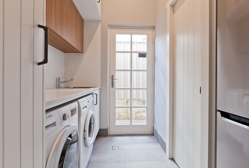 Photo of a small contemporary galley utility room in Perth with a built-in sink, light wood cabinets, engineered stone countertops, grey walls, porcelain flooring, a side by side washer and dryer, grey floors and white worktops.