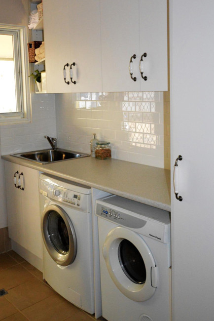 Foto på en liten funkis linjär tvättstuga, med vita skåp, laminatbänkskiva och vita väggar