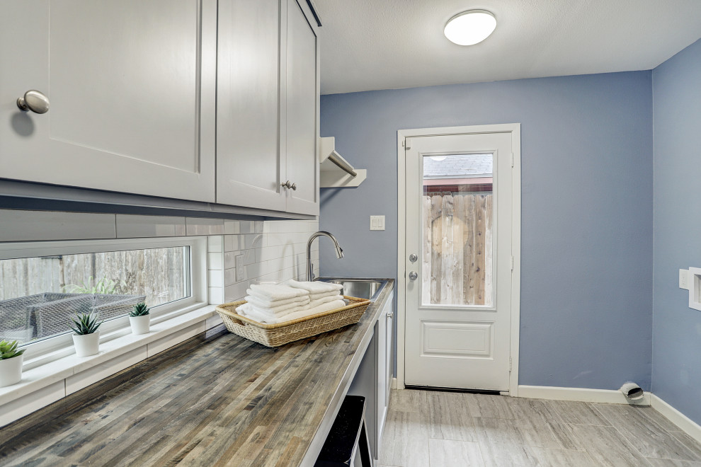 This is an example of a midcentury galley separated utility room in Houston with a single-bowl sink, shaker cabinets, grey cabinets, wood worktops, blue walls, porcelain flooring, a side by side washer and dryer and grey floors.