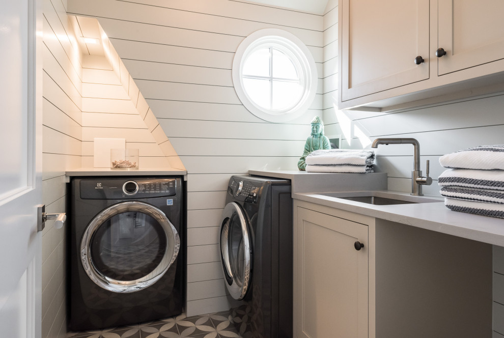 Example of a small beach style l-shaped ceramic tile and multicolored floor dedicated laundry room design in New York with an undermount sink, shaker cabinets, beige cabinets, solid surface countertops, white walls, a side-by-side washer/dryer and beige countertops