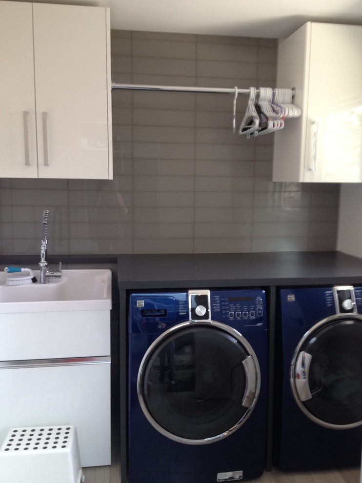 Zweizeilige, Kleine Moderne Waschküche mit Ausgussbecken, flächenbündigen Schrankfronten, weißen Schränken, Laminat-Arbeitsplatte, beiger Wandfarbe und Waschmaschine und Trockner nebeneinander in Calgary