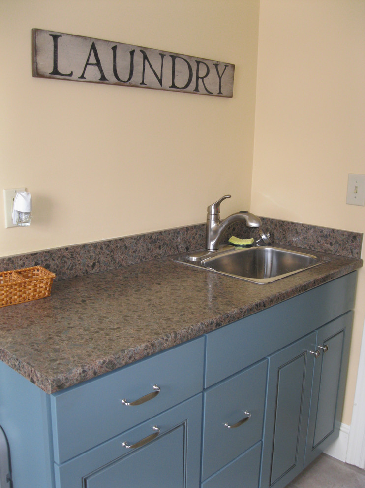 Immagine di una piccola lavanderia multiuso tradizionale con top in laminato, lavatrice e asciugatrice affiancate, lavello da incasso, pareti beige, pavimento in vinile e ante blu