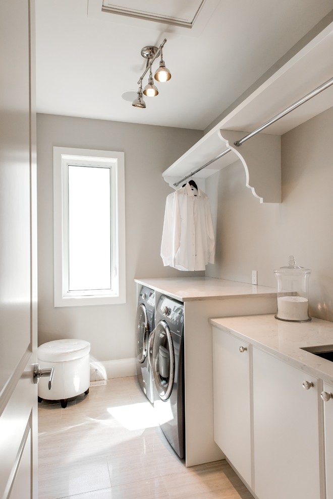 Foto på en mellanstor funkis linjär tvättstuga enbart för tvätt, med en undermonterad diskho, släta luckor, vita skåp, bänkskiva i kvarts, grå väggar, klinkergolv i porslin, en tvättmaskin och torktumlare bredvid varandra och beiget golv