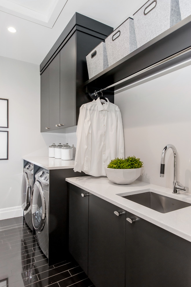 Photo of a large classic single-wall separated utility room in Calgary with a submerged sink, flat-panel cabinets, grey cabinets, engineered stone countertops, grey walls, ceramic flooring, a side by side washer and dryer and white worktops.
