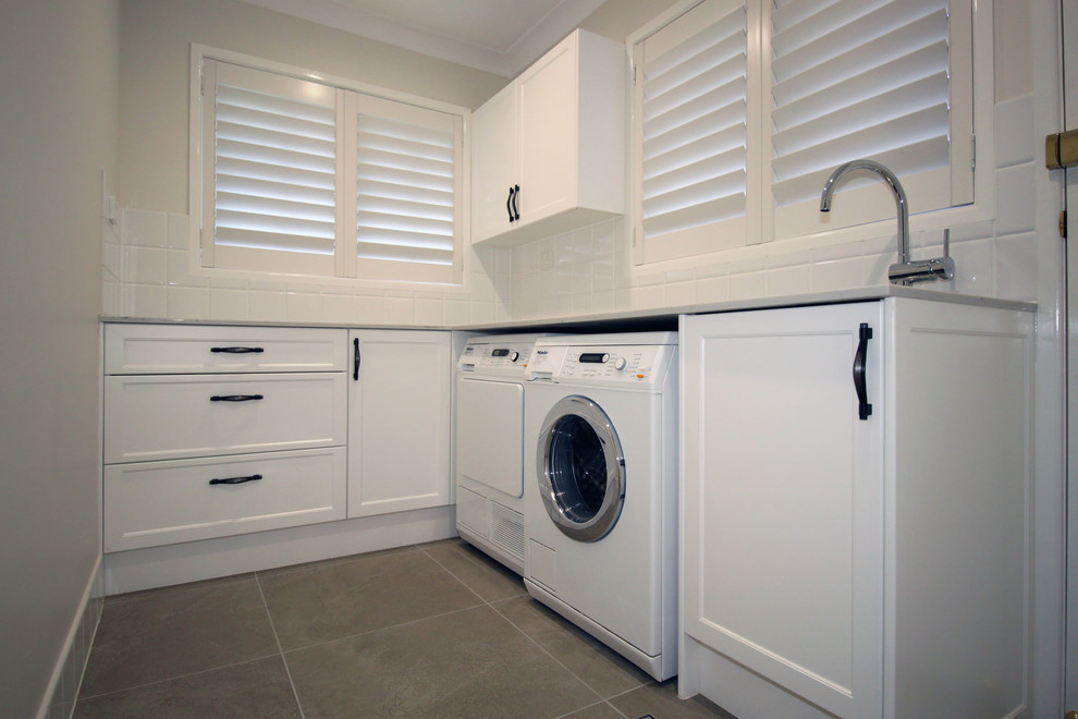 Idéer för en mellanstor klassisk grå l-formad tvättstuga enbart för tvätt, med en undermonterad diskho, skåp i shakerstil, vita skåp, bänkskiva i kvarts, vita väggar, klinkergolv i porslin, en tvättmaskin och torktumlare bredvid varandra och grått golv