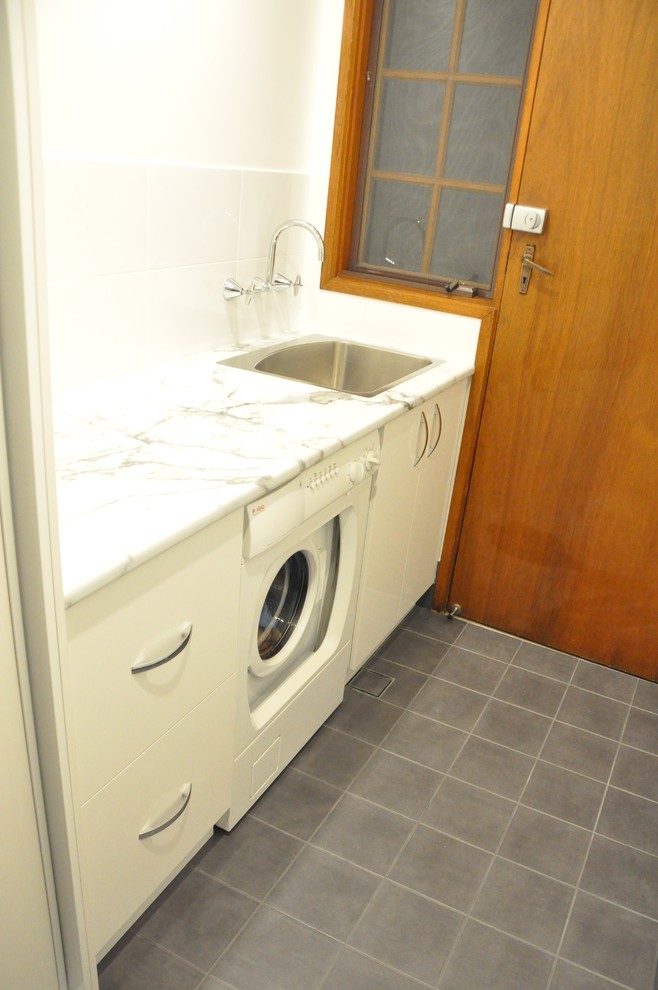 Foto di una piccola sala lavanderia minimalista con lavello da incasso, ante lisce, ante bianche, top in laminato, pareti bianche, pavimento con piastrelle in ceramica, lavatrice e asciugatrice nascoste e pavimento grigio