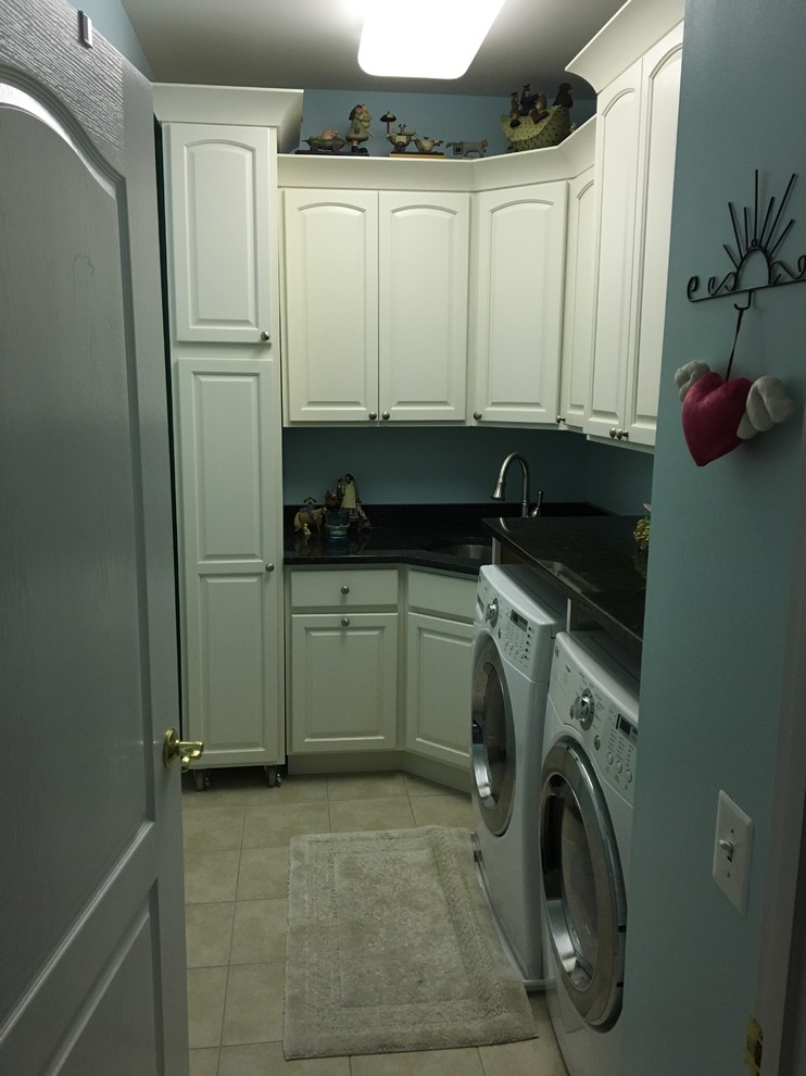 Inspiration for a mid-sized transitional l-shaped porcelain tile and beige floor dedicated laundry room remodel in Baltimore with white cabinets, an undermount sink, raised-panel cabinets, solid surface countertops, blue walls, a side-by-side washer/dryer and black countertops