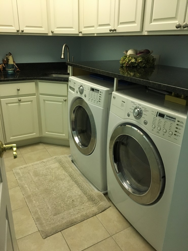 Inspiration for a mid-sized transitional l-shaped porcelain tile and beige floor dedicated laundry room remodel in Baltimore with white cabinets, an undermount sink, raised-panel cabinets, solid surface countertops, blue walls, a side-by-side washer/dryer and black countertops