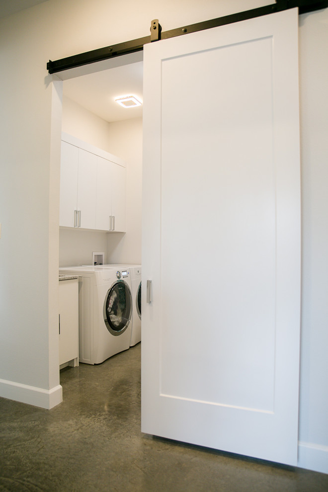 Inspiration för mellanstora moderna tvättstugor enbart för tvätt, med skåp i shakerstil, vita skåp, marmorbänkskiva, vita väggar, betonggolv och en tvättmaskin och torktumlare bredvid varandra