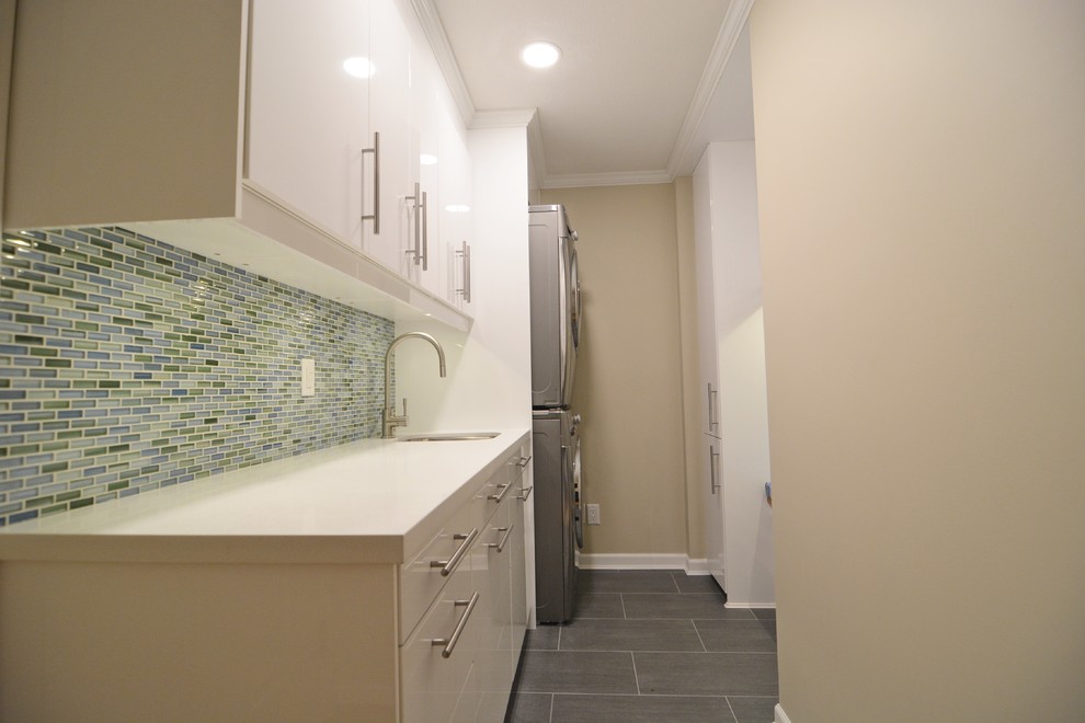 Photo of a small contemporary galley utility room in Vancouver with a submerged sink, flat-panel cabinets, white cabinets, engineered stone countertops, ceramic flooring, a stacked washer and dryer and beige walls.
