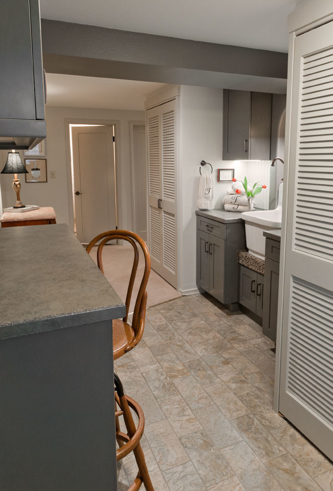Photo of a small traditional galley utility room in Seattle with a belfast sink, shaker cabinets, grey cabinets, laminate countertops, grey walls, vinyl flooring and a stacked washer and dryer.