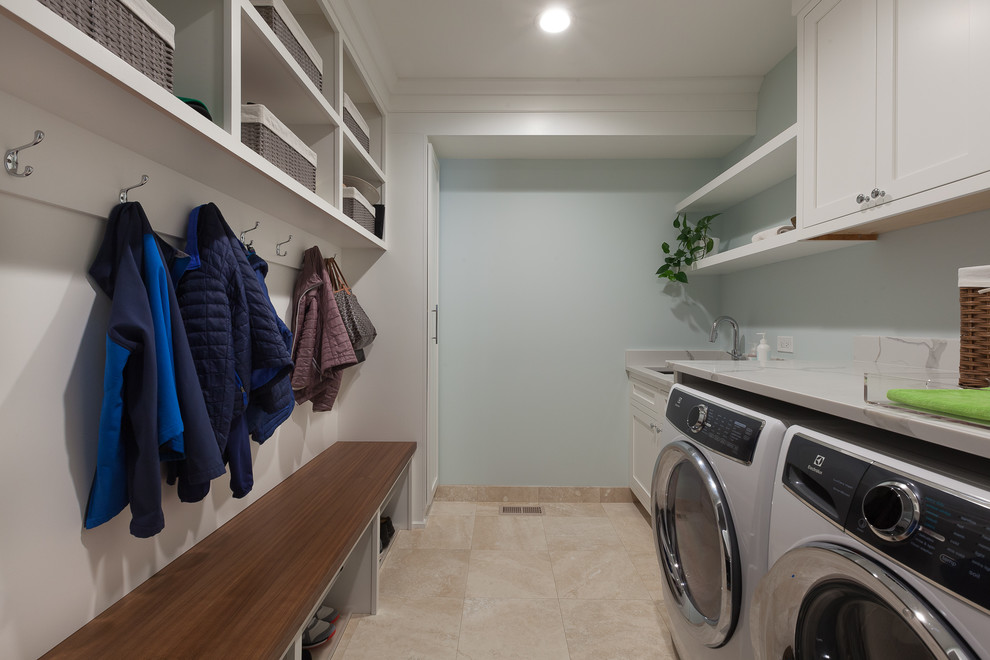 シカゴにあるお手頃価格の中くらいなトランジショナルスタイルのおしゃれな家事室 (コの字型、アンダーカウンターシンク、シェーカースタイル扉のキャビネット、白いキャビネット、クオーツストーンカウンター、青い壁、大理石の床、左右配置の洗濯機・乾燥機、ベージュの床、グレーのキッチンカウンター) の写真