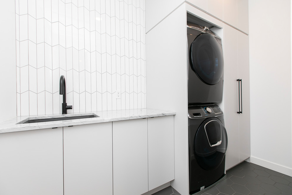 This is an example of a medium sized single-wall separated utility room in Ottawa with a submerged sink, flat-panel cabinets, grey cabinets, marble worktops, white walls, ceramic flooring, a stacked washer and dryer, grey floors and grey worktops.