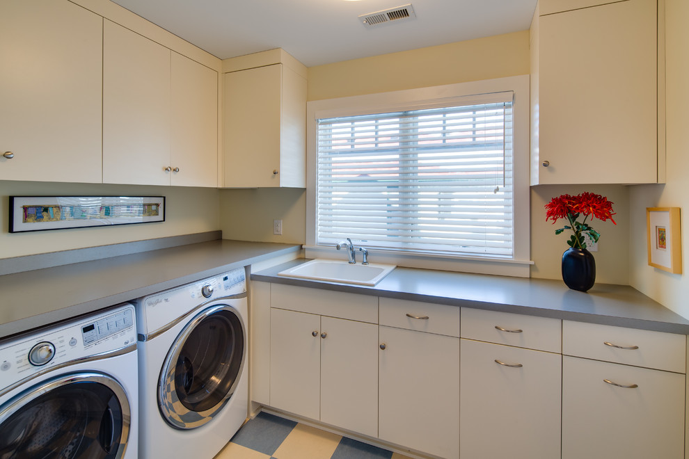 ミネアポリスにある高級な中くらいなトラディショナルスタイルのおしゃれな洗濯室 (L型、ドロップインシンク、フラットパネル扉のキャビネット、白いキャビネット、ラミネートカウンター、黄色い壁、リノリウムの床、左右配置の洗濯機・乾燥機) の写真