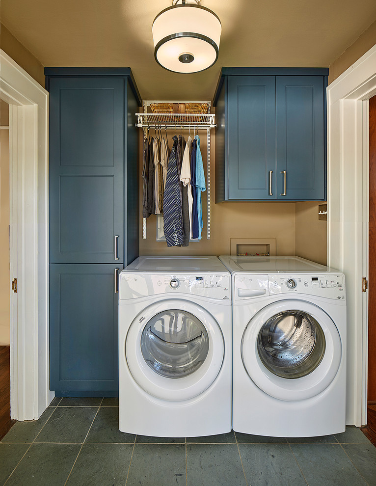 Exempel på en liten amerikansk linjär tvättstuga enbart för tvätt, med skåp i shakerstil, blå skåp, skiffergolv, en tvättmaskin och torktumlare bredvid varandra, grått golv och bruna väggar