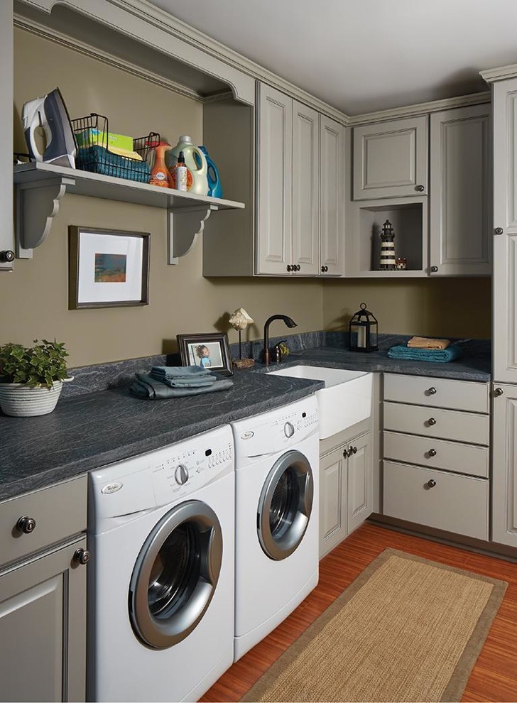 Inredning av en klassisk mellanstor grå l-formad grått tvättstuga enbart för tvätt, med en rustik diskho, luckor med upphöjd panel, grå skåp, bänkskiva i täljsten, beige väggar, mellanmörkt trägolv och en tvättmaskin och torktumlare bredvid varandra